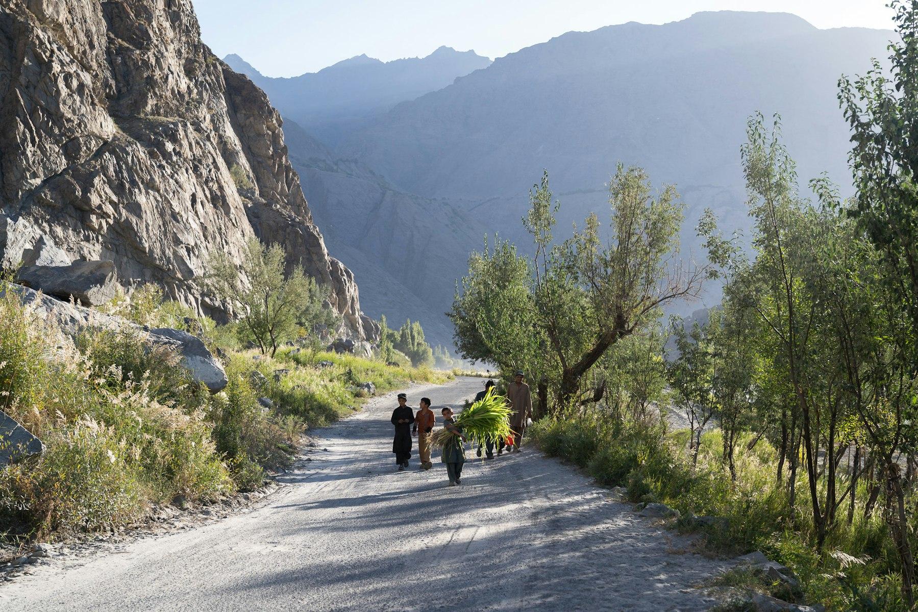 People walk along a mountain path, carrying crops and other items.