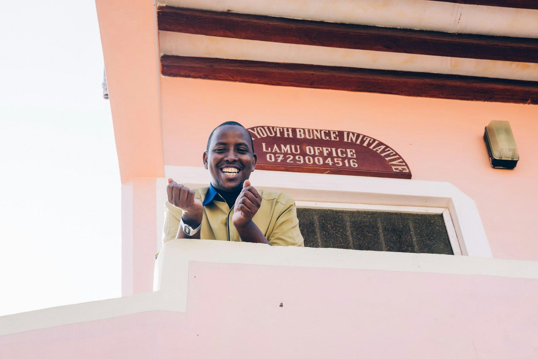 The director of a youth group in Lamu, Kenya, looks down from the balcony of a pink-painted building.