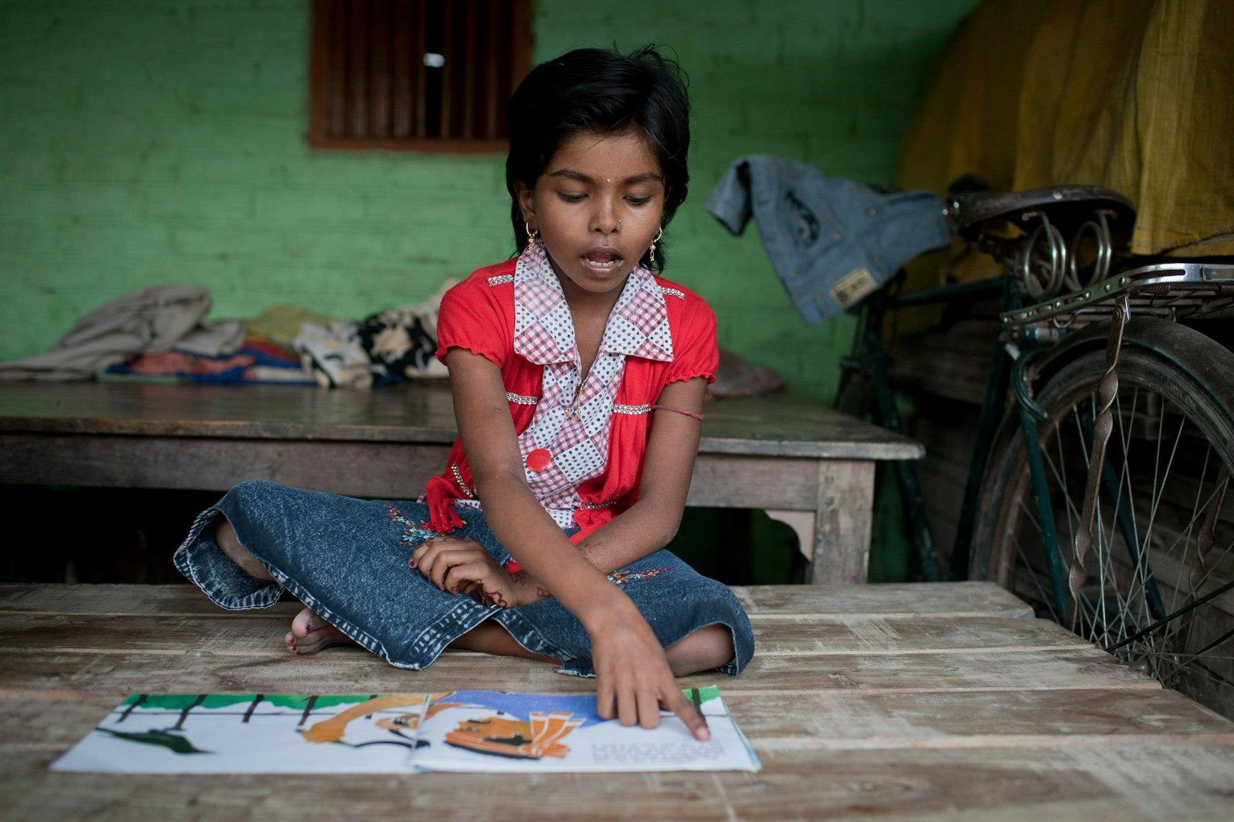 A cross-legged girl reads aloud from a picturebook.