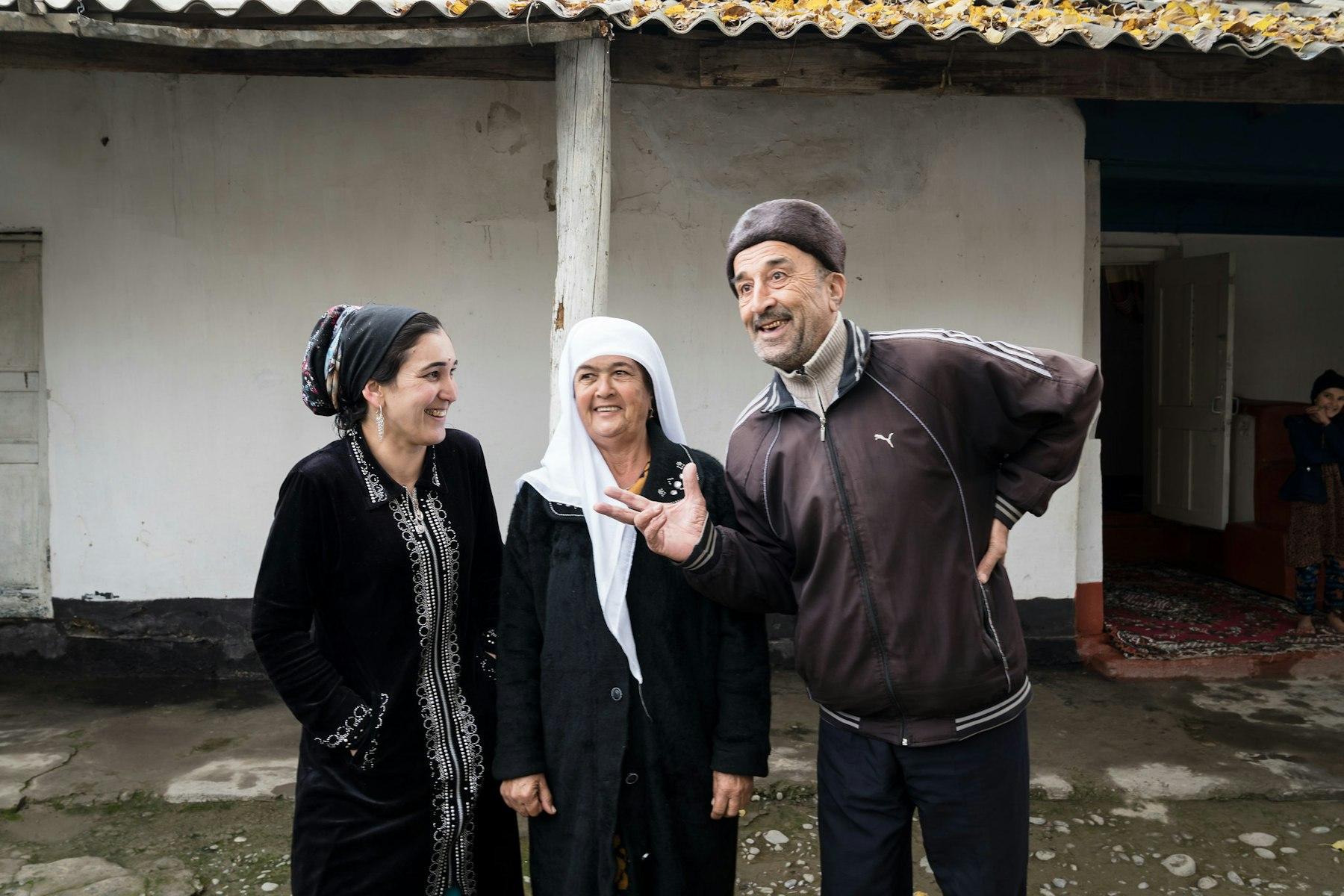 A man and two women stand laughing in front of a house.