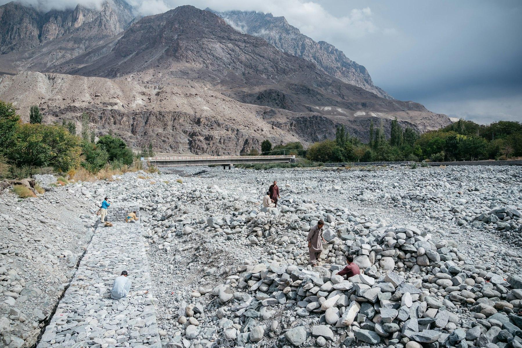 Men surrounded by grey stones build walls in a valley.