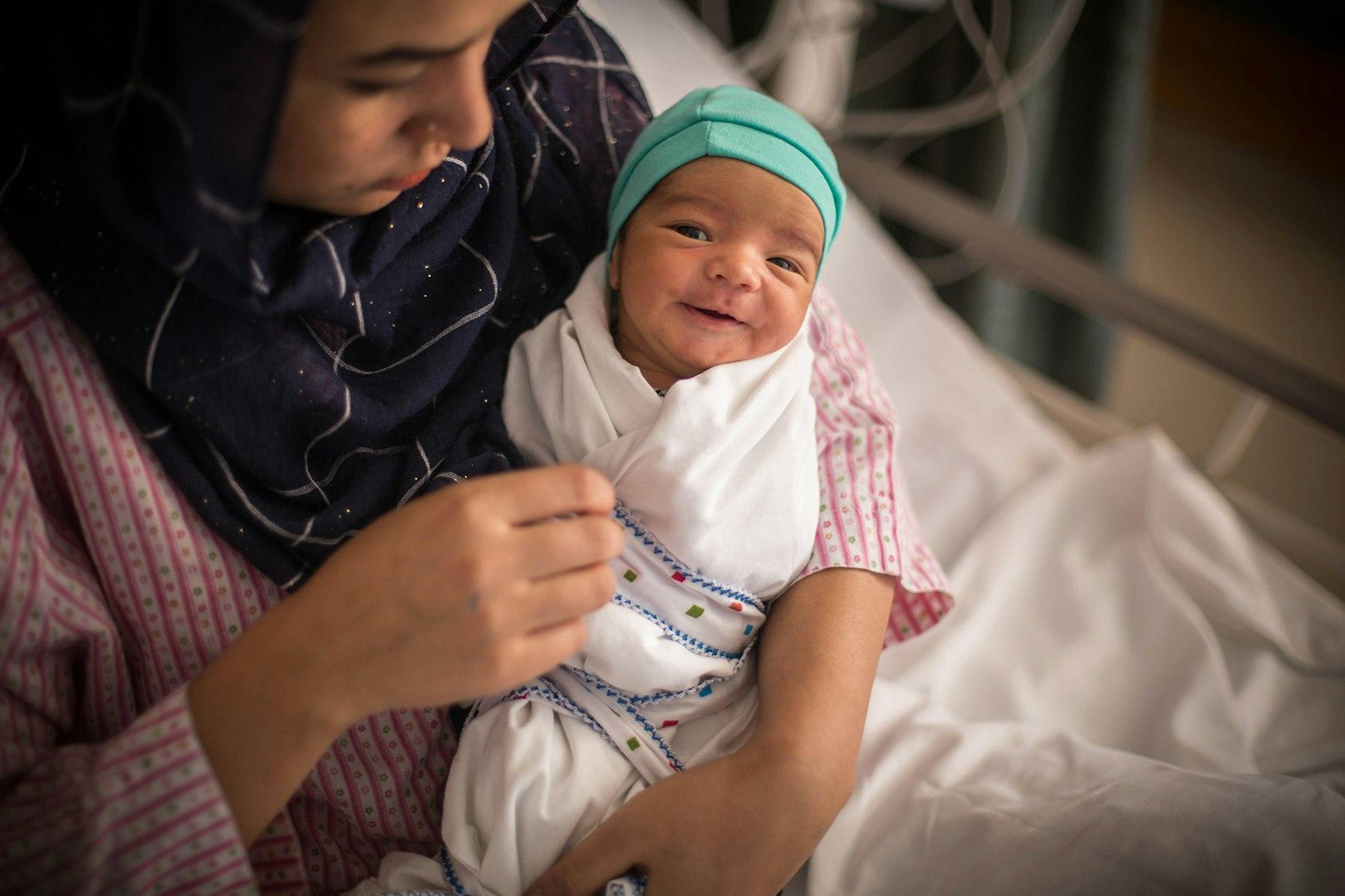 Uma mulher numa cama de hospital segura um bebé pequeno.