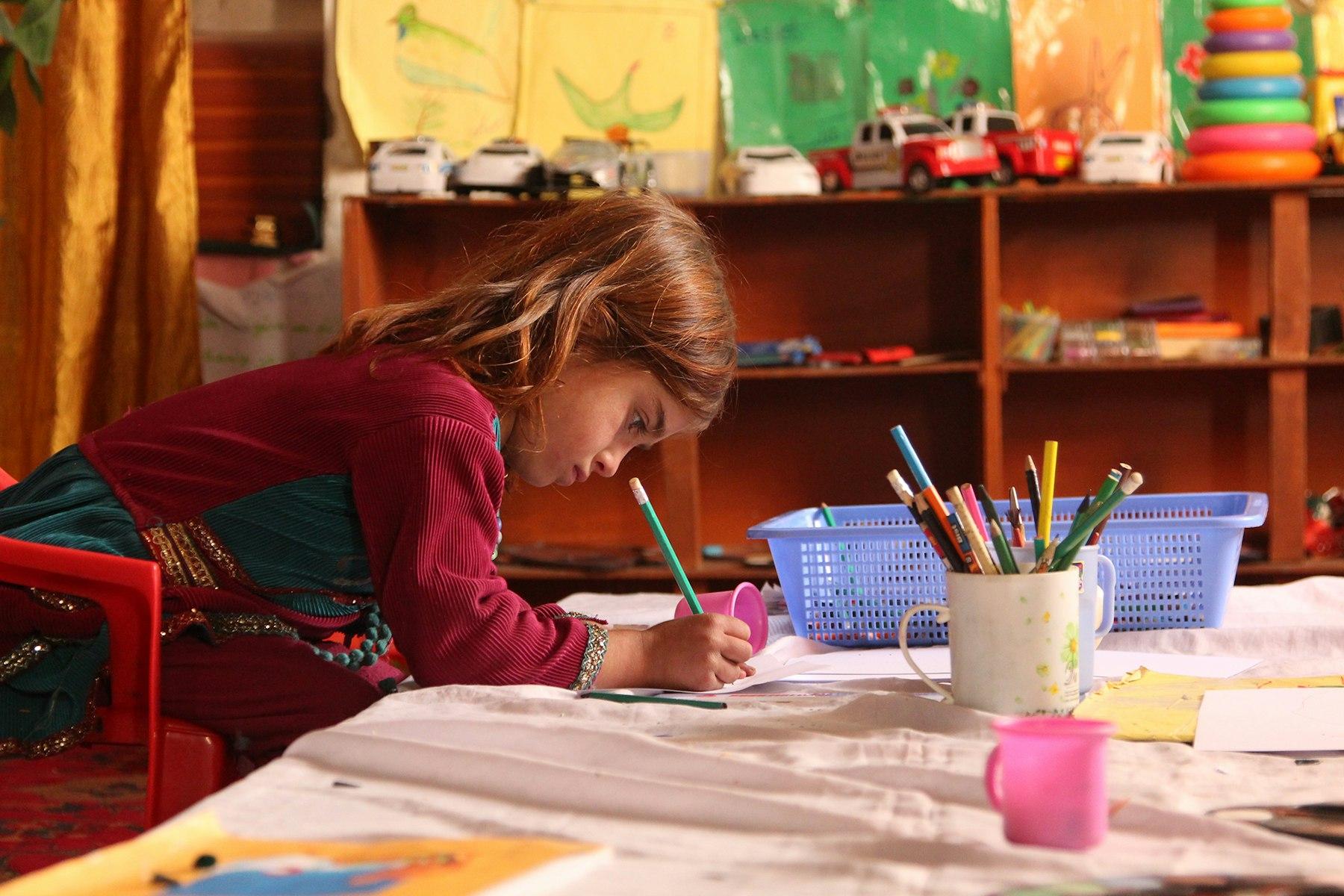 A young student leans over a table to write with a pencil.