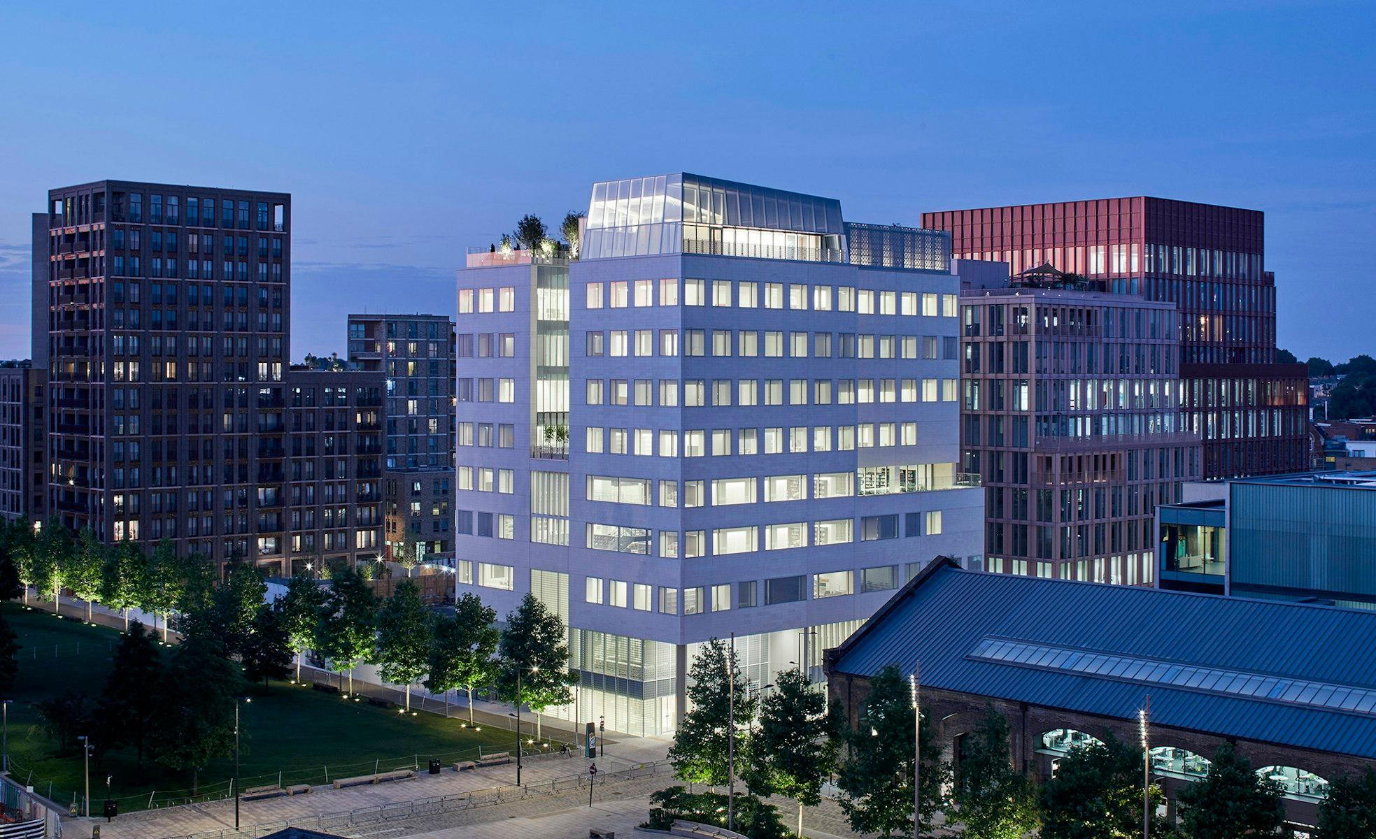 Exterior view of the Aga Khan Centre, a white building lit from within. Other office buildings are adjacent.