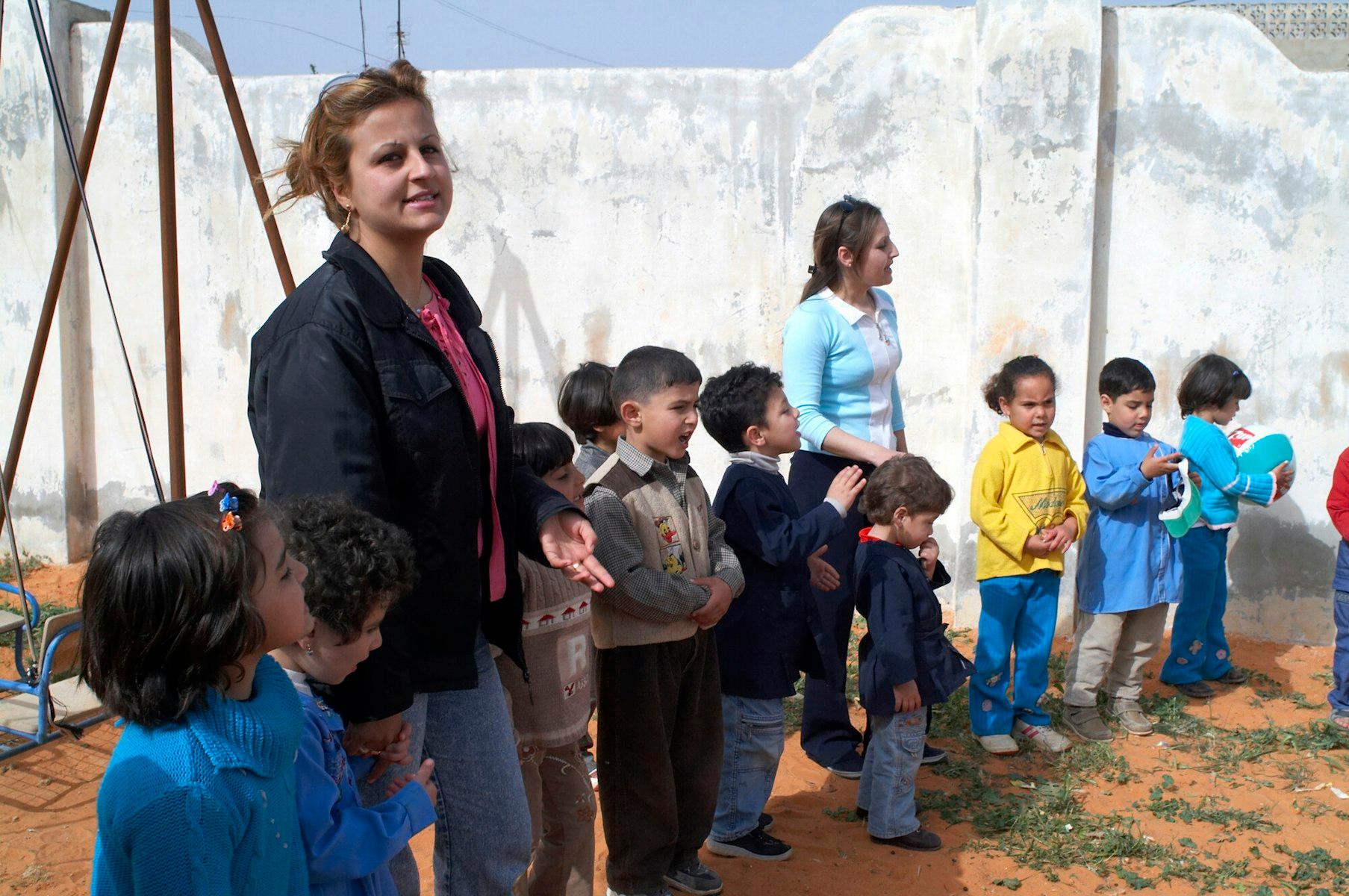 Des enfants se tiennent en rang avec leurs enseignantes sur un terrain de jeu.