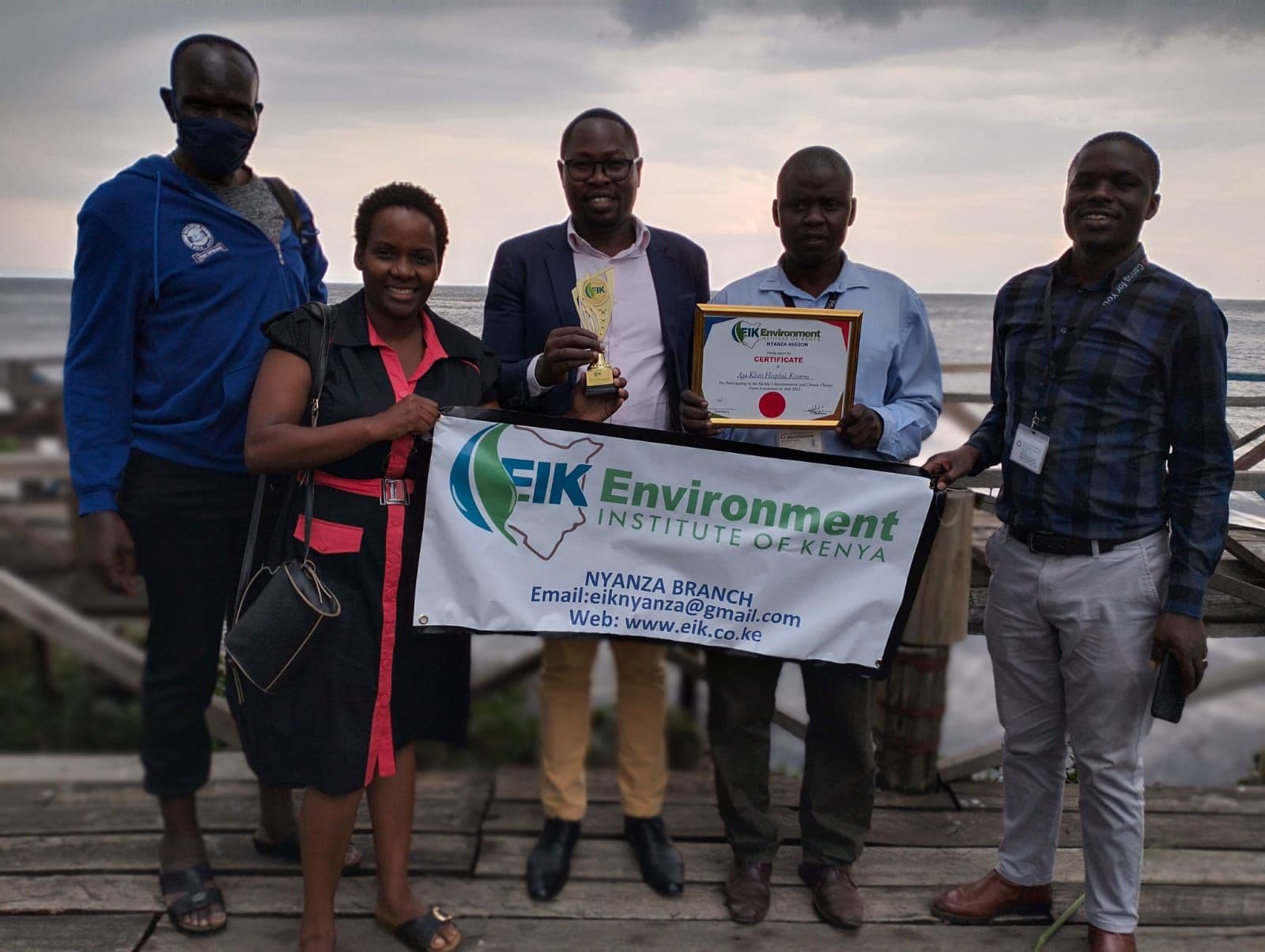 A row of five people hold up a framed award and an EIK banner.