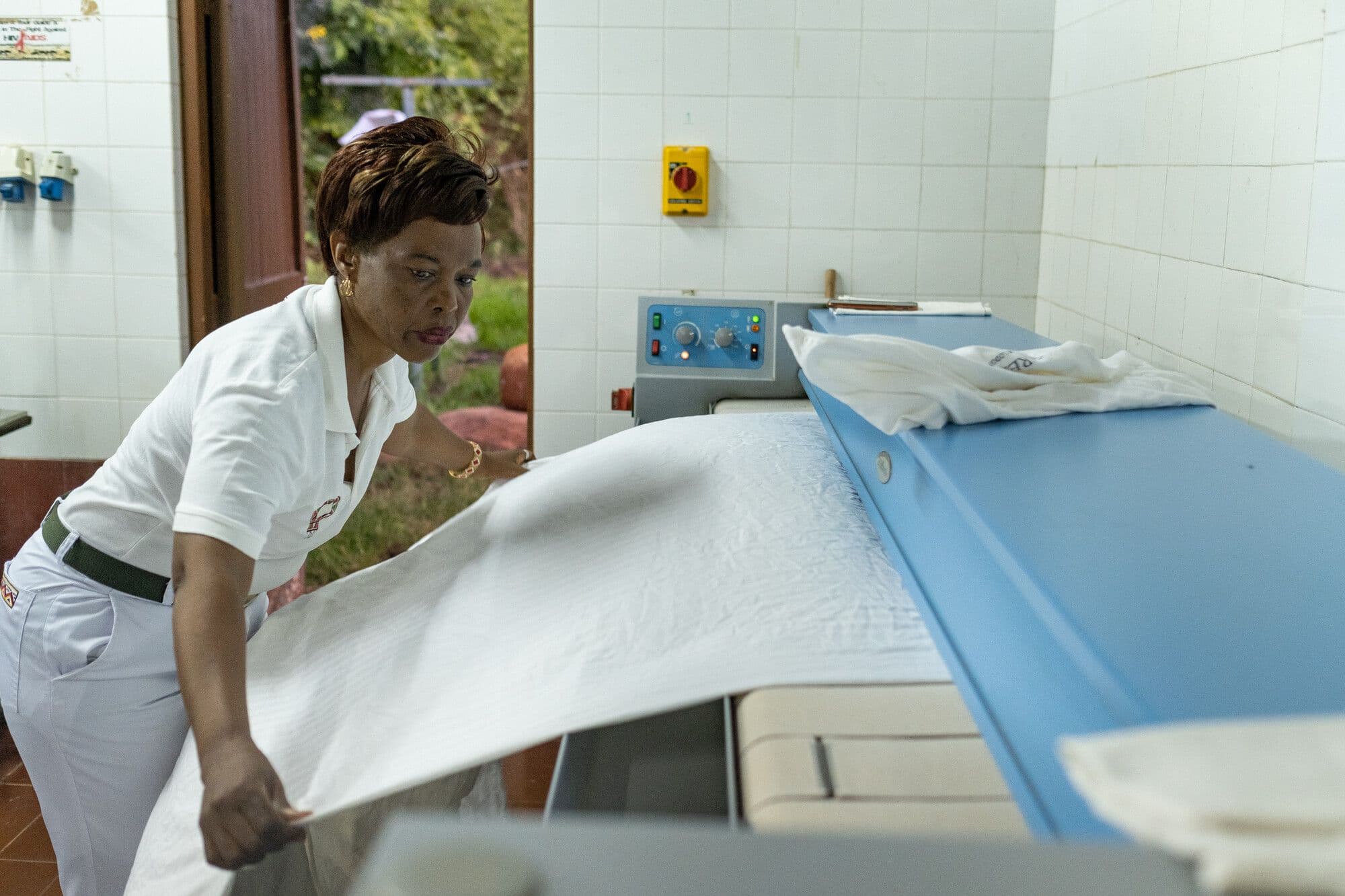 A woman in a white uniform puts cloth through the laundry.